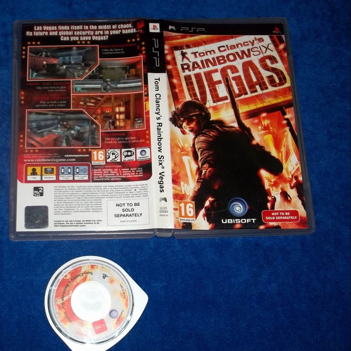 Tom Clancy's Rainbow Six Vegas video game for PSP, showing the game case with its outer and inner sleeves, plus the included game disc, laid out on a blue textured fabric background.