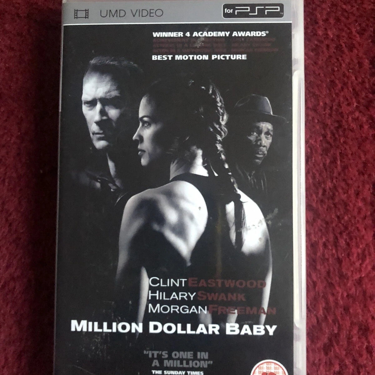 A VHS case for the movie 'Million Dollar Baby' with Clint Eastwood, Hilary Swank, and Morgan Freeman, photographed on a textured red fabric background.