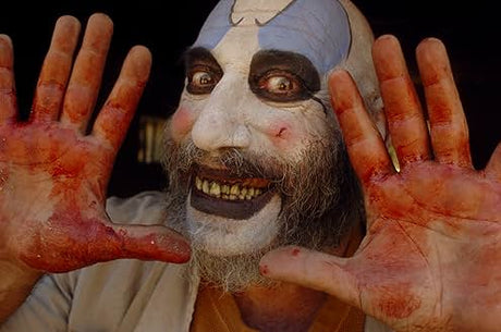 Person wearing a mask with painted face and hands showing red paint, against a dark background