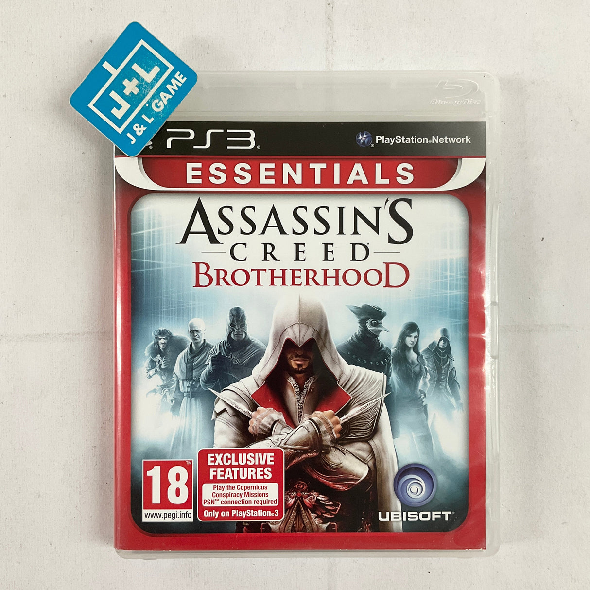 PS3 game case for Assassin's Creed Brotherhood Essentials, shown in a clear plastic sleeve with a blue J&L Game sticker on the top left, photographed against a light neutral background.