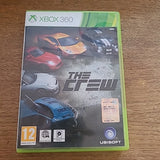 The Crew video game case for Xbox 360, featuring a lime green plastic case with a cover showing several sports cars and the Xbox 360 and Ubisoft logos, placed on a wooden surface.