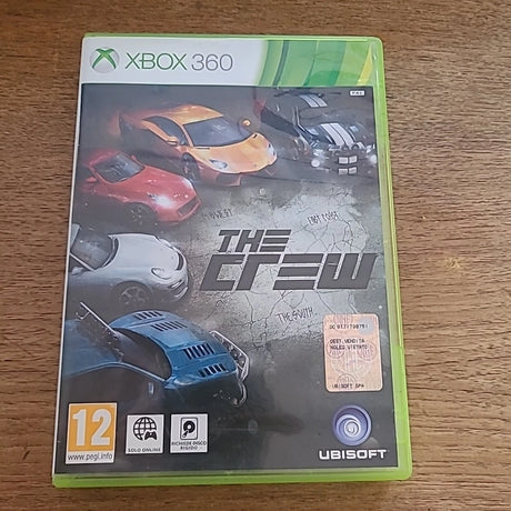The Crew video game case for Xbox 360, featuring a lime green plastic case with a cover showing several sports cars and the Xbox 360 and Ubisoft logos, placed on a wooden surface.