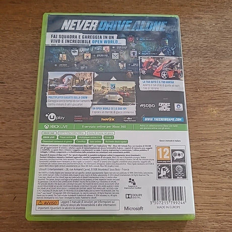 Back cover of a Never Drive Alone Xbox 360 game case, photographed on a wooden surface. Visible branding includes Microsoft, Xbox, Asobo Games, and The Tech Game.